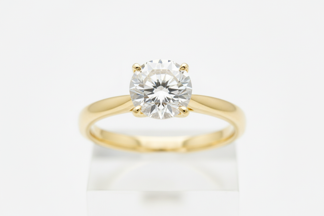 Close-up of a round diamond solitaire ring on a yellow gold band against a neutral background.