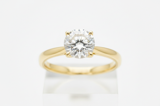 Close-up of a round diamond solitaire ring on a yellow gold band against a neutral background.
