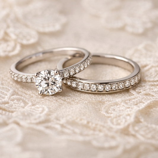 Engagement ring and matching wedding band side by side on lace fabric, showing flush fit with pavé diamonds under soft lighting.