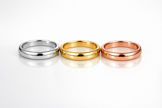 White gold, yellow gold and rose gold rings lined up on a reflective white surface with soft lighting