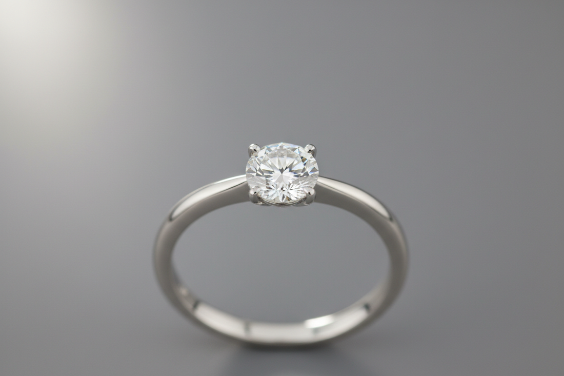 Close-up of a solitaire diamond engagement ring with a plain band under soft studio lighting