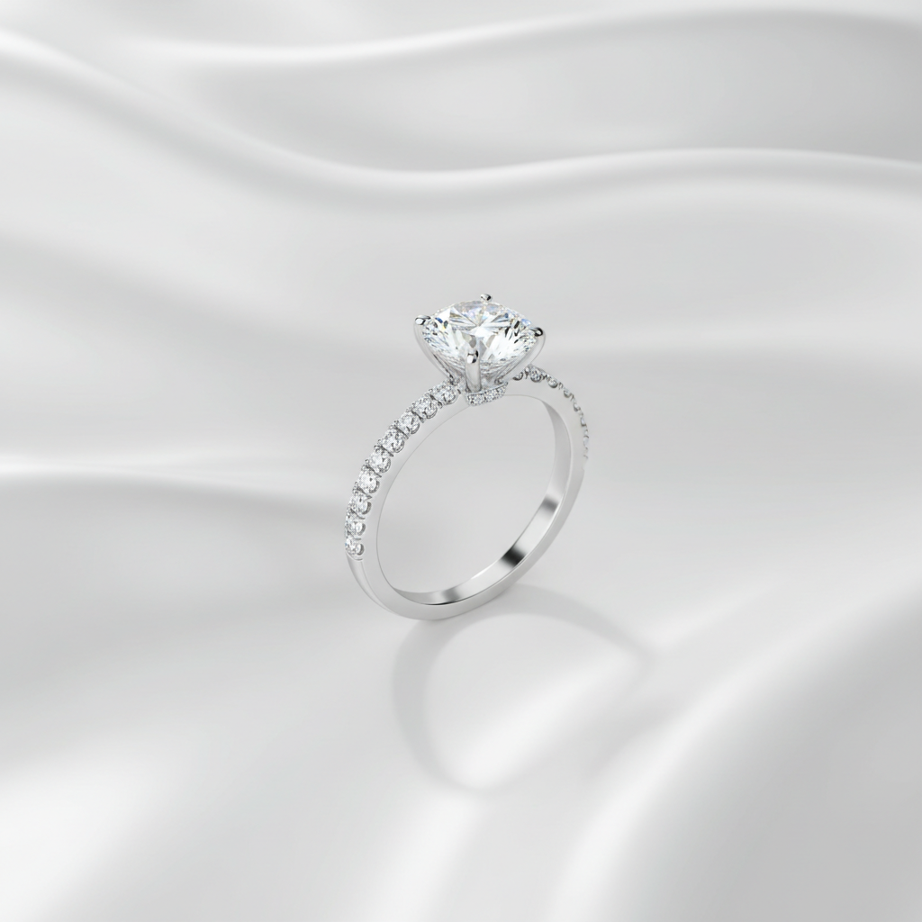 Close-up of a pave diamond engagement ring with a round centre stone on a white gold band against a silky white background.