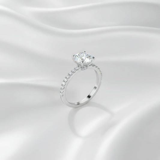 Close-up of a pave diamond engagement ring with a round centre stone on a white gold band against a silky white background.