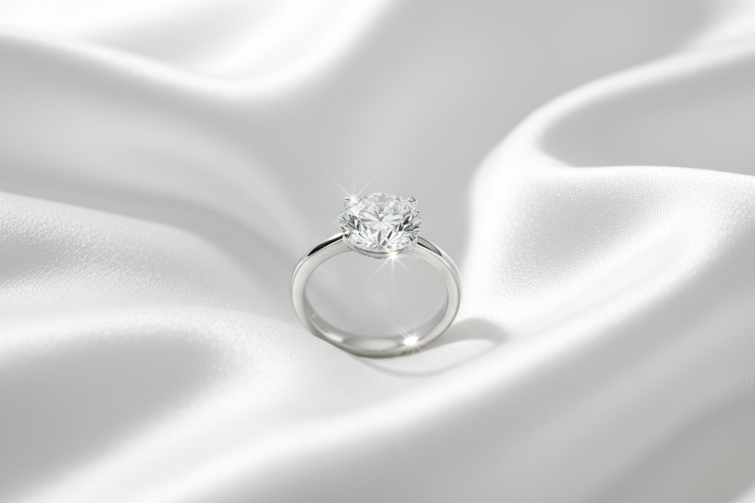 Close-up of a round diamond solitaire ring on a white gold band resting on a silk fabric with a neutral background.