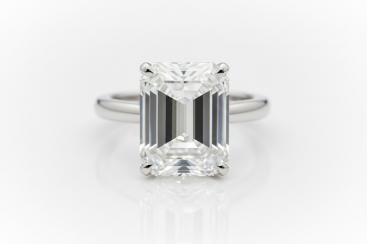 Close-up of an emerald-cut diamond solitaire engagement ring on a white gold band against a neutral background.